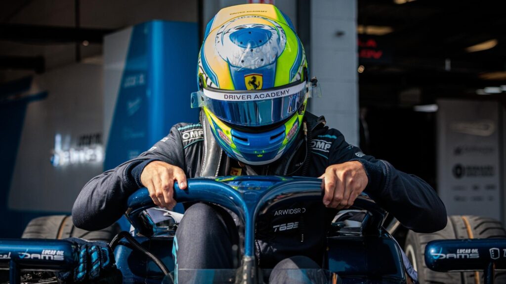Dino Beganovic kliver i sin blå DAMS-bil med hjälmen på, med händerna på halobågen. Ferrari Driver Academy-loggan syns på hjälmen.