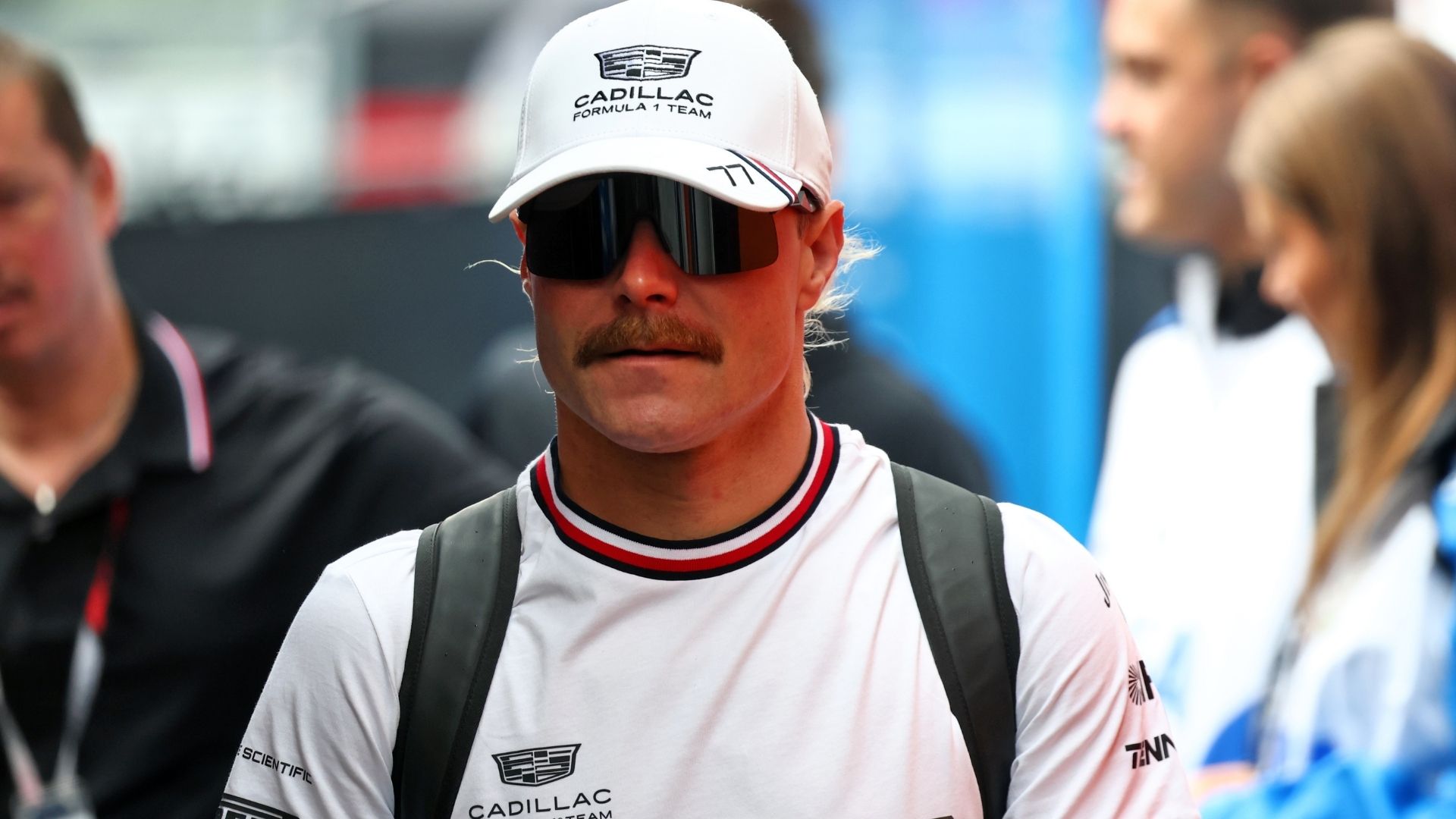 Valtteri Bottas i Cadillacs vita teamkläder och keps med solglasögon i Formel 1-paddocken.